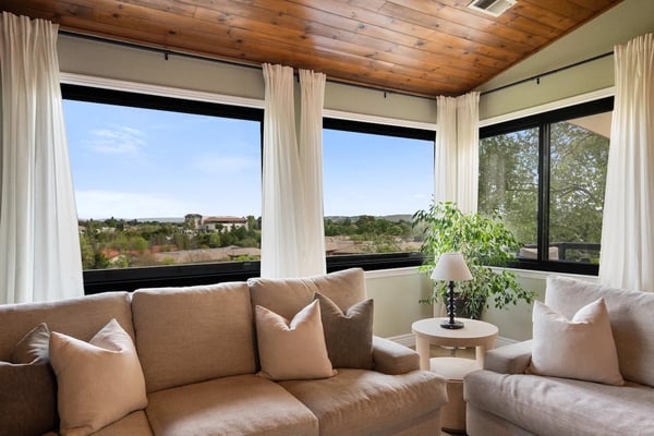 Sunroom with beige sectional sofa, wooden ceiling, and large windows overlooking rolling hills and countryside.